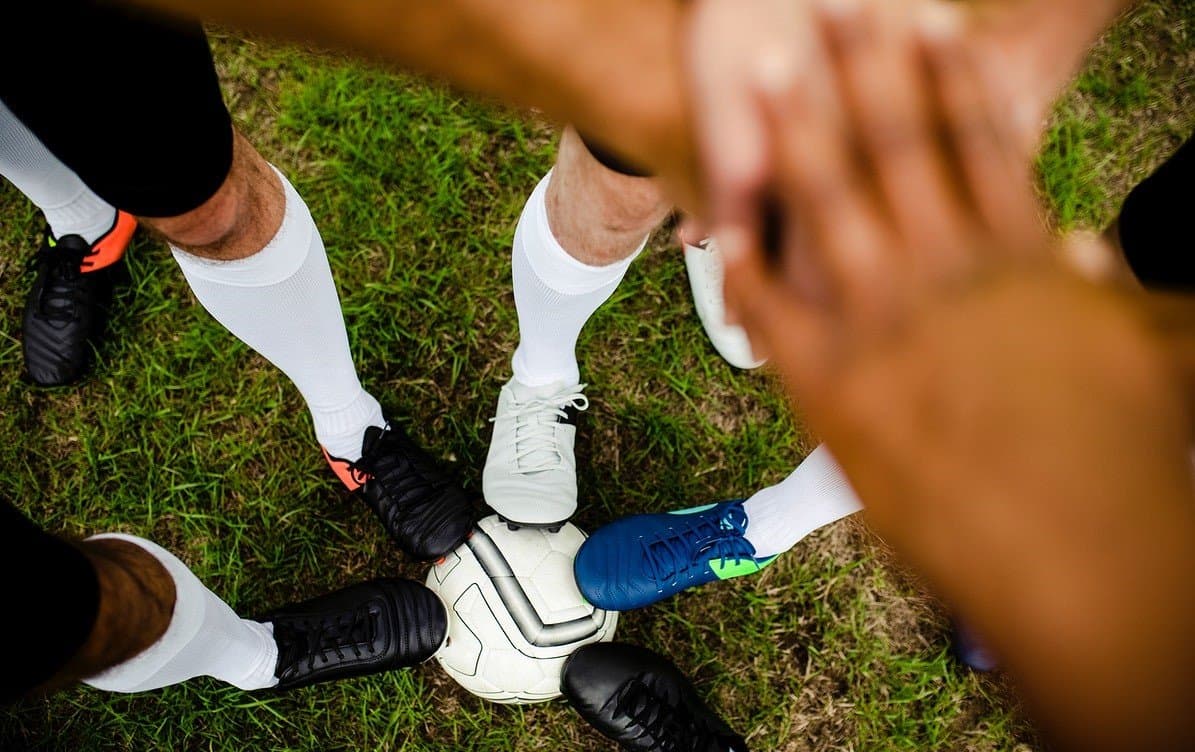 Soccer players stacking hands in a team huddle above their cleats and a ball
