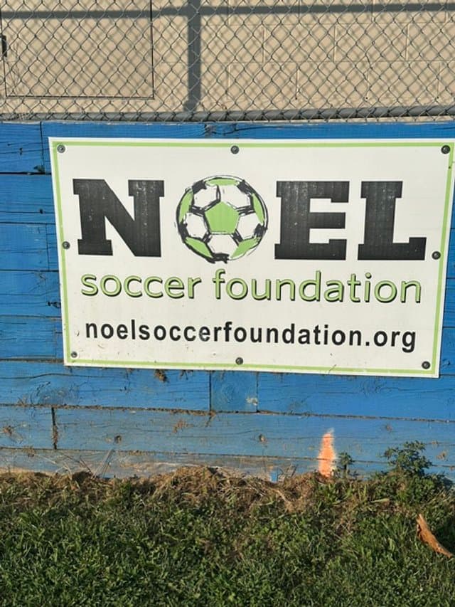 Noel Soccer Foundation sign on the fence at the Lighthouse Soccer Club field